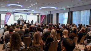 Ein Publikum schaut auf eine Leinwand. Darauf sieht man Lukas Britschgi, der live dazugeschaltet wurde.