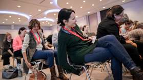 Personen sitzen im Publikum. Sie greifen unter ihren Stuhl. Darunter ist ein Laneyard befestigt.