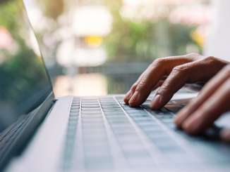 Blick auf die Tastatur eines Laptops. Die Finger tippen darauf.