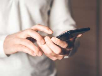 Eine Person hält ein Handy in den Händen und trägt einen weissen Pullover.