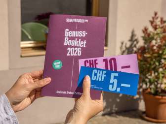 Eine Person hält das Genuss-Booklet in die Luft. Eine Broschüre mit Genusstipps und Gutscheinen zum Einlösen.