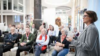 Eine Frau steht vor einem kleinen Publikum und referiert.