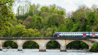 Ein Zug der SBB fährt vom rechten Bildrand über die Rheinfall Brücke.