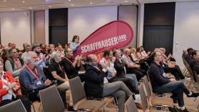 Eine Person trägt eine Beachflag mit dem Schaffhauserland Logo durchs Publikum.